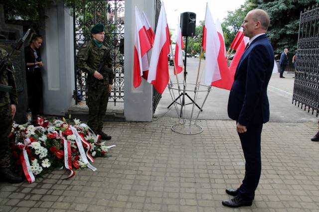 Zastępca burmistrza Dariusz Tracz podczas składania wiązanki kwiatów pod pamiątkową tablicą.